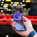 Close-up of a modern flip smartphone held in hand, showcasing innovative technology outdoors in a bustling city.