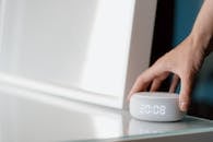 Close-up of a hand adjusting a smart speaker displaying time indoors.